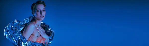 A woman in a silver jacket poses against a bright blue background. — Stock Photo