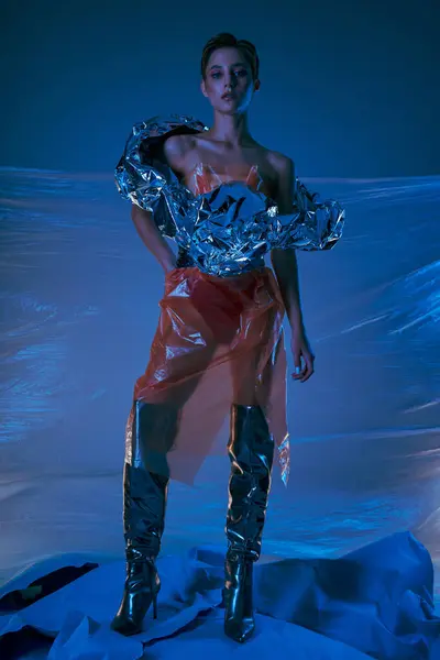 A woman wearing a shimmering, recycled fashion piece stands against a backdrop of plastic sheeting. — Stock Photo