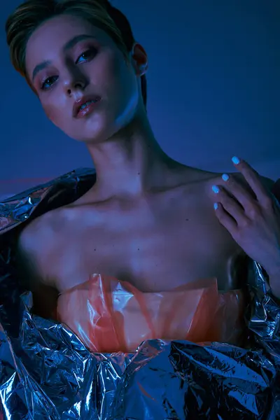 A woman wearing a shimmering pink top draped in silver fabric poses against a blue backdrop. — Stock Photo