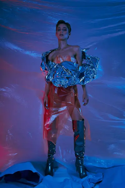 Uma mulher em uma roupa futurista está contra um pano de fundo azul e vermelho feito de plástico. — Fotografia de Stock