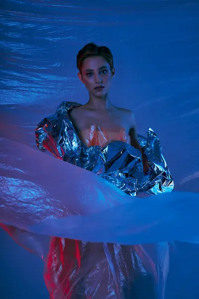 A woman in a shimmering silver garment poses under ethereal blue light. — Stock Photo