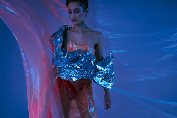 Uma mulher vestindo uma prata, roupas de moda sustentável posa na frente de um pano de fundo azul e rosa. — Fotografia de Stock