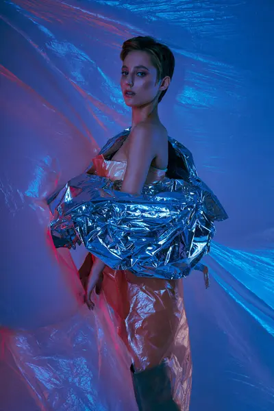 Una mujer posa sobre un fondo azul, envuelta en una tela plateada y brillante. — Stock Photo