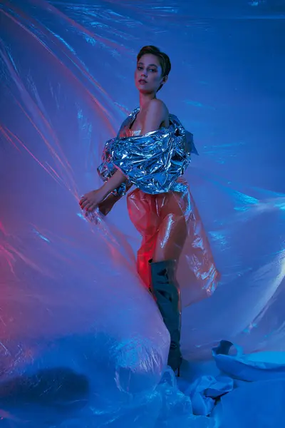 A woman wearing a silver jacket and red pants stands surrounded by blue and pink plastic. — Stock Photo