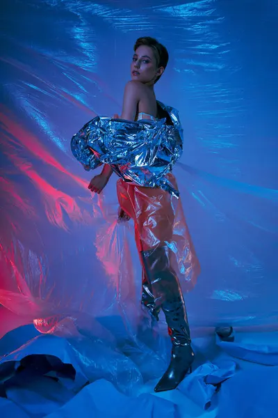 A woman in a silver jacket and black boots poses amidst a swirling sea of blue and red plastic. — Stock Photo
