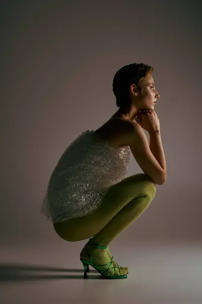 A woman in green tights sits with her chin in her hands. She is wrapped in a sheet of bubble wrap. — Stock Photo