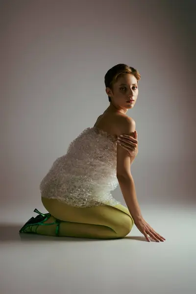 Una mujer con un atuendo de moda sostenible se arrodilla sobre un telón de fondo liso. — Stock Photo