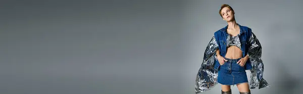 Woman in denim stands against gray backdrop, donning matching jacket and skirt with silver trim — Stock Photo