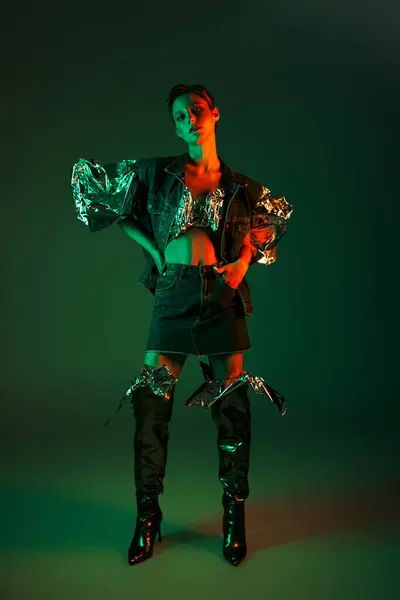 Mulher em trajes de ganga posa no fundo verde, iluminado por luzes de néon, ostentando estilo sustentável — Fotografia de Stock