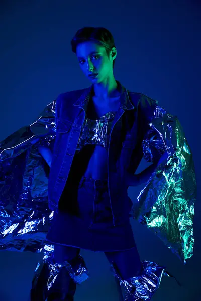 Woman in blue jacket with silver accents stands in vibrant blue and green lit studio — Stock Photo