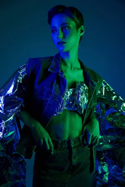 Uma mulher posa em uma roupa de moda sustentável sob iluminação azul e verde vibrante. — Fotografia de Stock