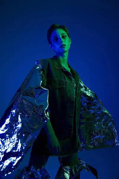 A woman wears a sustainable fashion garment of silver fabric under blue and green lighting. — Stock Photo
