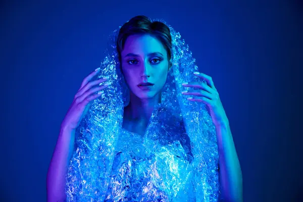 A woman poses in a studio bathed in blue light, wearing a garment made from recycled materials. — Stock Photo
