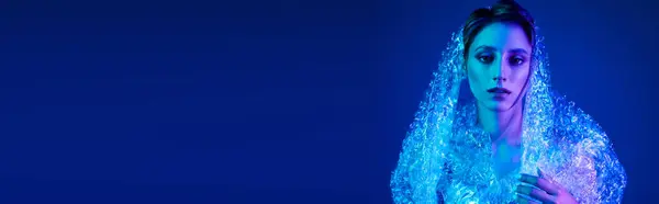 A woman, bathed in blue light, stands enveloped in a shimmering, sustainable fabric. — Stock Photo