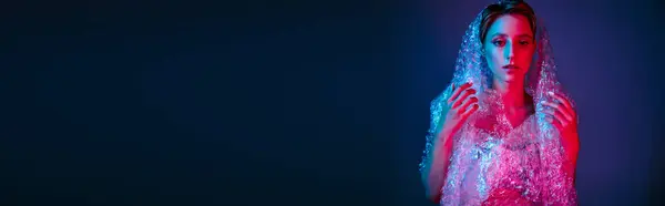 Uma mulher em um vestido de plástico está contra um fundo escuro, iluminado por luzes vermelhas e azuis. — Fotografia de Stock