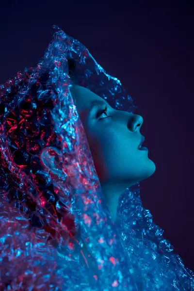 A woman with long, dark hair is enveloped in bubble wrap, illuminated by blue and red lights. — Stock Photo