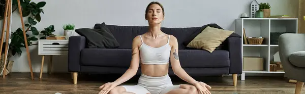 A young woman with vitiligo sits in a lotus position on a wooden floor, eyes closed, practicing yoga in a modern apartment. — Stock Photo