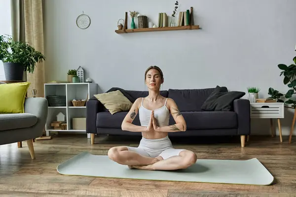 Eine junge Frau mit Vitiligo meditiert in einer modernen Wohnung und sitzt in Yoga-Pose auf einer Matte. — Stockfoto