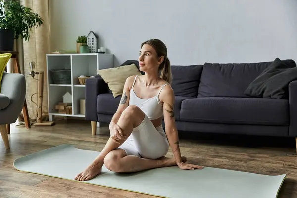 Une jeune femme pratique le yoga sur un tapis dans un salon moderne, avec un canapé en arrière-plan. — Photo de stock