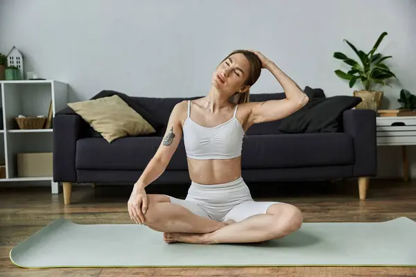 Una joven con vitiligo se sienta en una esterilla de yoga en un apartamento moderno, practicando una pose de yoga, centrándose en su respiración y bienestar mental. — Stock Photo