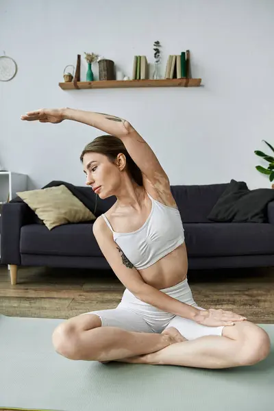 A young woman in active wear practices yoga on a mat in her living room. — Stock Photo