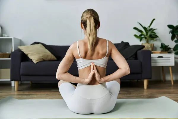 A young woman in active wear practices yoga in a modern apartment. She sits in a meditative pose with her hands clasped behind her back. — Stock Photo