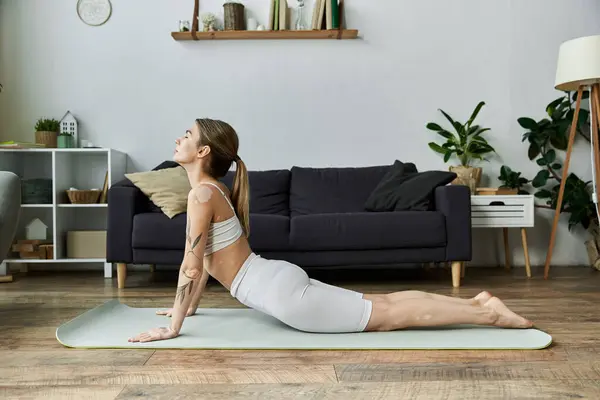 A young woman in activewear practices yoga on a mat in a modern apartment. — Stock Photo
