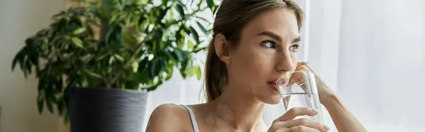 A young woman in activewear sits near a window in a modern apartment, drinking water after practicing yoga. — Stock Photo