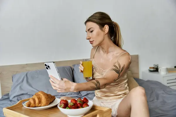 A young woman with vitiligo and a tattoo enjoys her breakfast in bed, taking a moment to check her phone. — Stock Photo