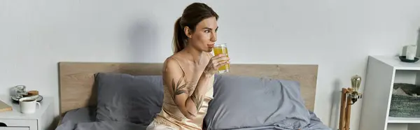 A young woman with vitiligo and a tattoo sits on her bed, enjoying a drink in her cozy bedroom. — Stock Photo