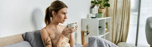 A young woman with vitiligo and a tattoo relaxes on her bed, enjoying a cup of coffee in her modern apartment. — Stock Photo