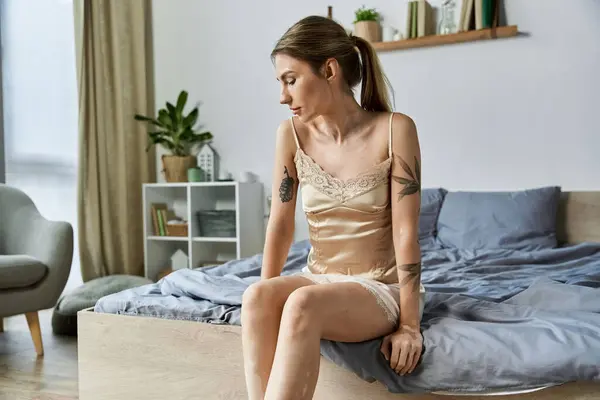 A young woman with vitiligo sits on the edge of a bed in her apartment, lost in thought. — Stock Photo