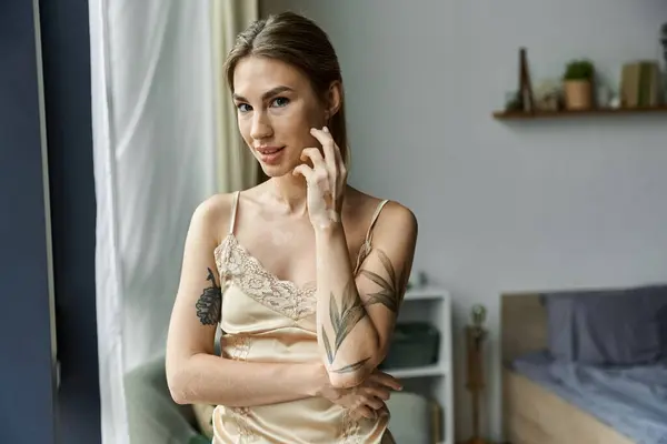 A young woman with vitiligo and tattoos stands in her cozy bedroom, looking directly at the camera. — Stock Photo