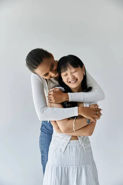 Um casal lésbico inter-racial abraça em um momento terno, sua felicidade irradiando contra um simples pano de fundo cinza. — Fotografia de Stock