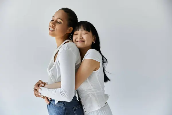 A young African American and Asian lesbian couple embrace each other, eyes closed, in a moment of intimacy against a gray background. — Stock Photo