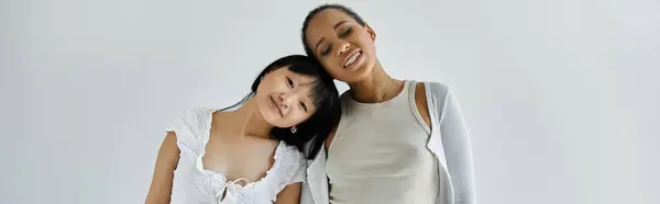 Two young women lean against each other in a tender embrace against a grey backdrop. — Stock Photo