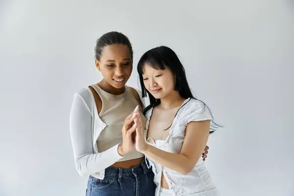 Two young women, one Black and one Asian, share a tender moment together against a white backdrop. — Stock Photo