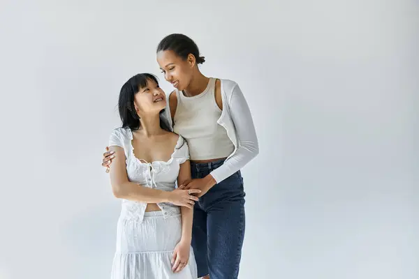 An interracial lesbian couple gazes lovingly at each other against a simple white background. — Stock Photo