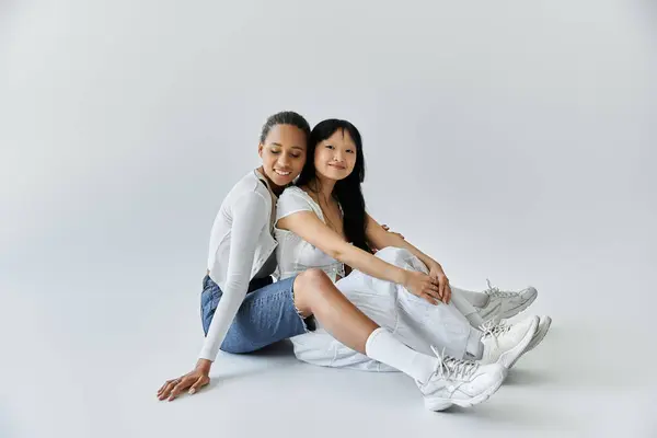 Two women, one African American and one Asian, embrace on a white floor — Stock Photo