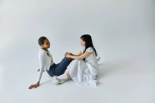 A young African American woman and an Asian woman share a tender moment while sitting on a white floor. — Stock Photo