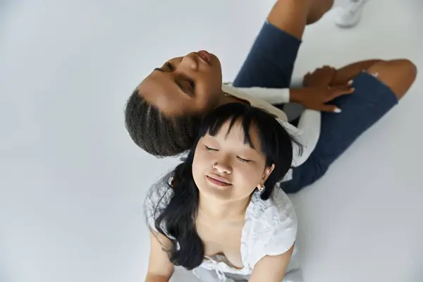 An African-American woman and an Asian woman, both young, lay together on a gray background, eyes closed in a tender moment. — Stock Photo