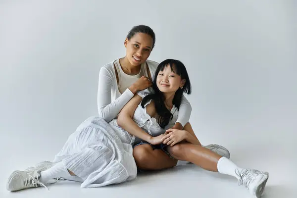 A young, interracial lesbian couple shares a tender moment together on a soft gray background. — Stock Photo