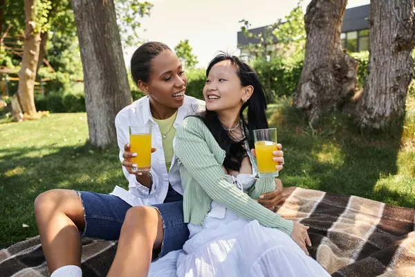An interracial lesbian couple enjoys a sunny picnic in the park, sharing drinks and smiles. — Stock Photo