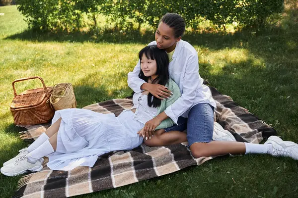 A lesbian couple enjoys a picnic together, embracing on a checkered blanket in a grassy park. — Stock Photo
