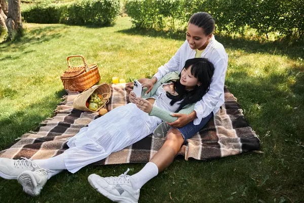 A young lesbian couple enjoys a picnic in the park, laughing and looking at their phones. — Stock Photo