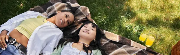 Two young women, one Black and one Asian, share a peaceful moment on a blanket in a sunny park, immersed in nature beauty — Stock Photo