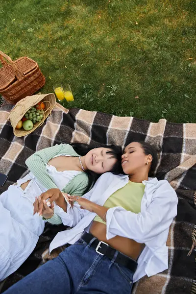 Two young women lie together on a blanket, holding hands and enjoying a picnic in the sun. — Stock Photo