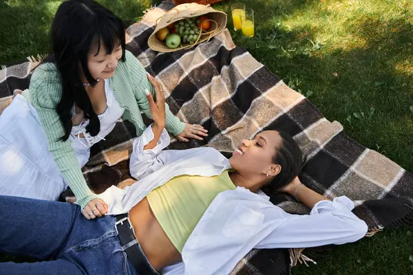 Duas jovens mulheres relaxam em um cobertor de piquenique em um parque gramado, aproveitando o dia ensolarado. — Fotografia de Stock