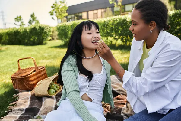 Two young women enjoy a picnic on a sunny day, sharing a piece of fruit and a moment of intimacy. — Stock Photo