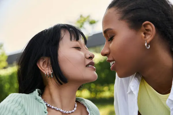 Two young women, one Asian and one African American, look at each other with affection during a picnic. — Stock Photo